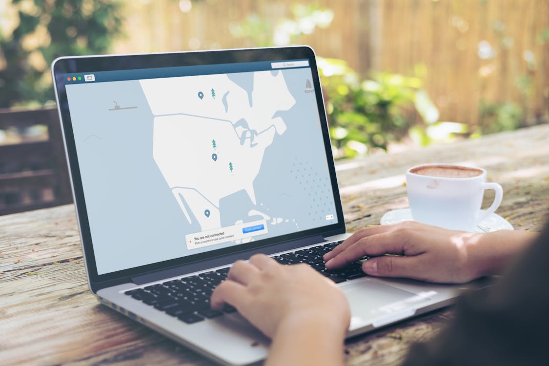 Free Person Using Black and Gray Laptop Computer Beside White Ceramic Cup on Brown Wooden Table Stock Photo