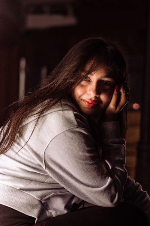 Free Portrait of a smiling woman with long brunette hair, wearing a white sweater, in warm indoor lighting. Stock Photo