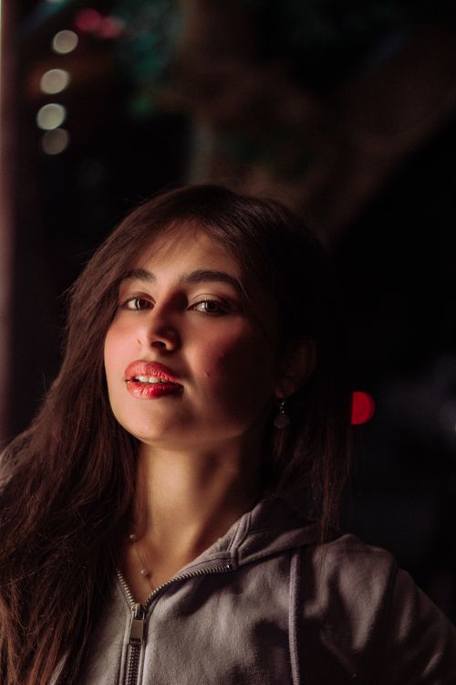 Free Portrait of a brunette woman posing outdoors at night in a gray hoodie, lit by soft lights. Stock Photo
