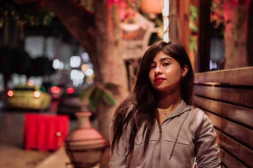 Free A woman sitting on a wooden bench in an urban setting during evening hours. Stock Photo
