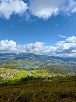 Scenic view of rolling hills and a small village under a vibrant blue sky in Pontevedra, Spain.