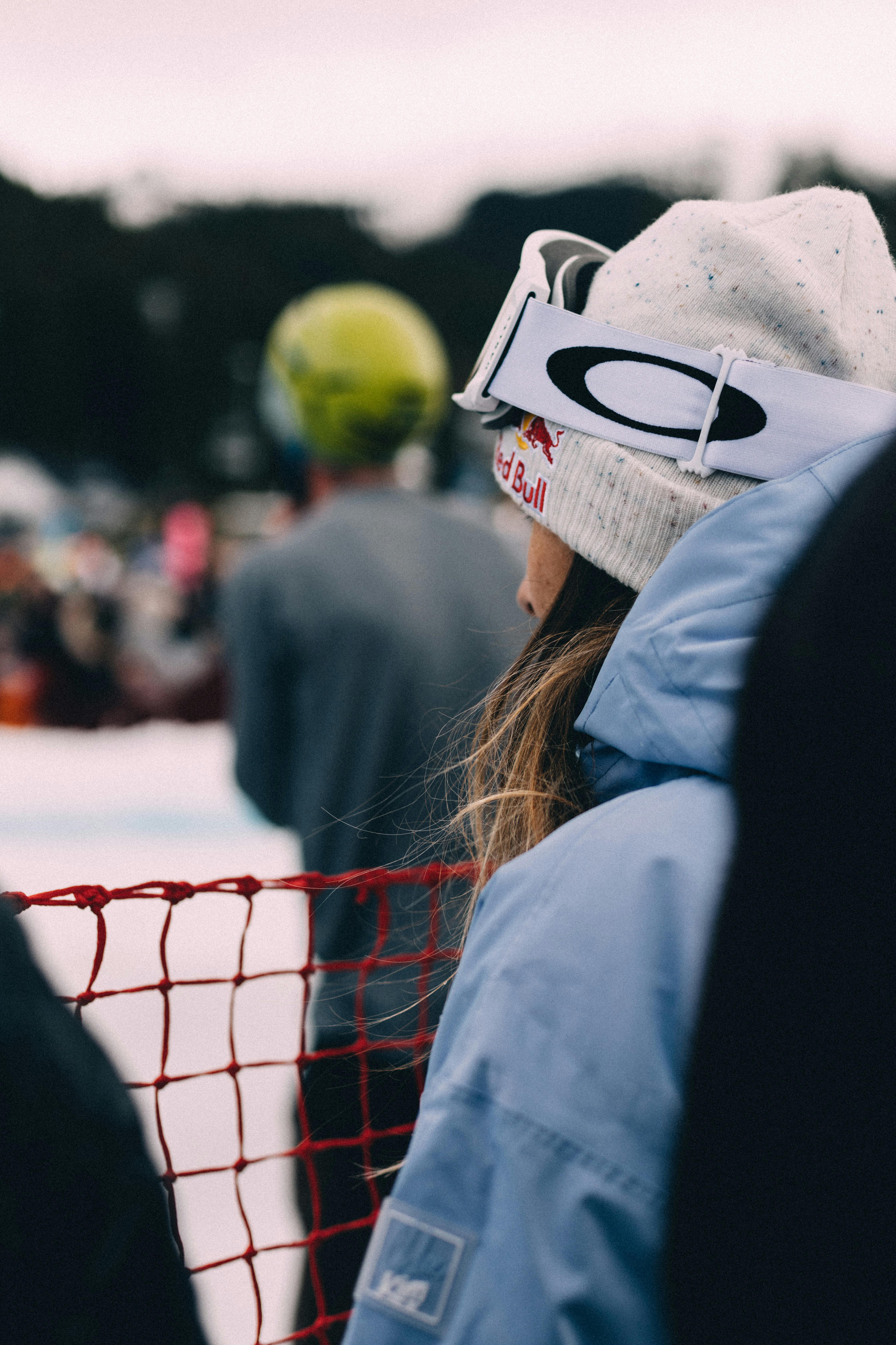 Prescription Goggle Inserts - Woman in winter clothing watching a skiing competition from the sidelines with focus on goggles and snowy ambiance.