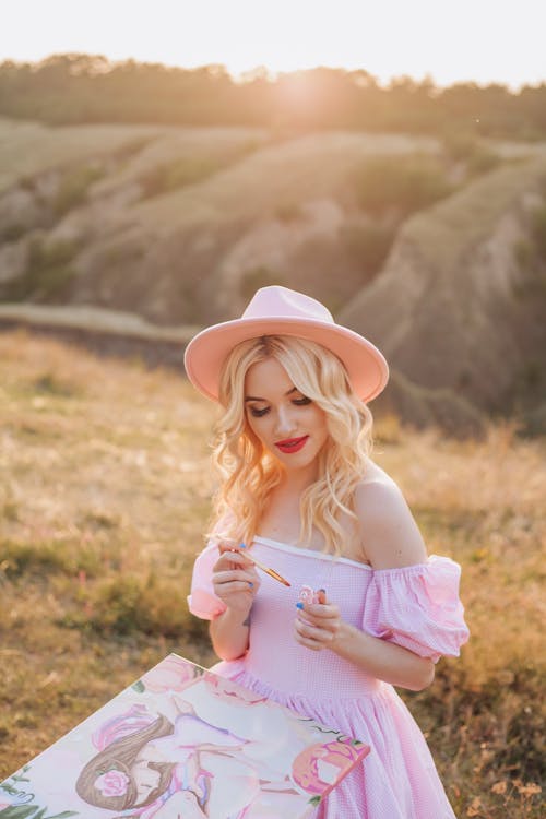 Blonde Woman in Hat Sitting and Drawing at Sunset
