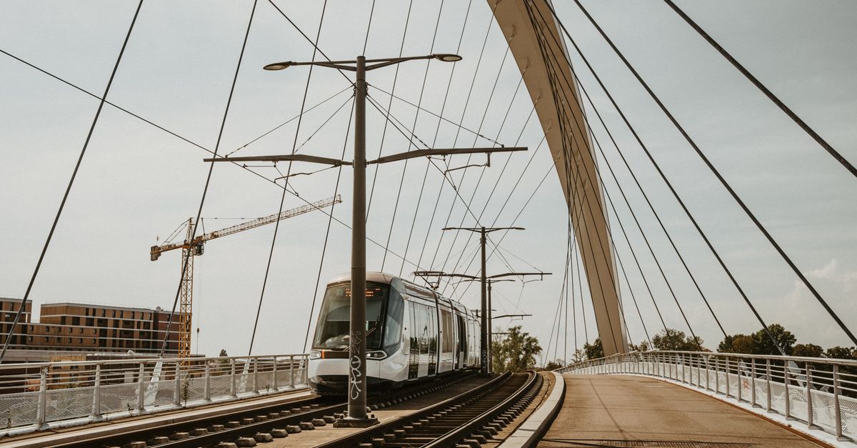 A sleek tram traverses a contemporary cable-stayed bridge in an urban setting.