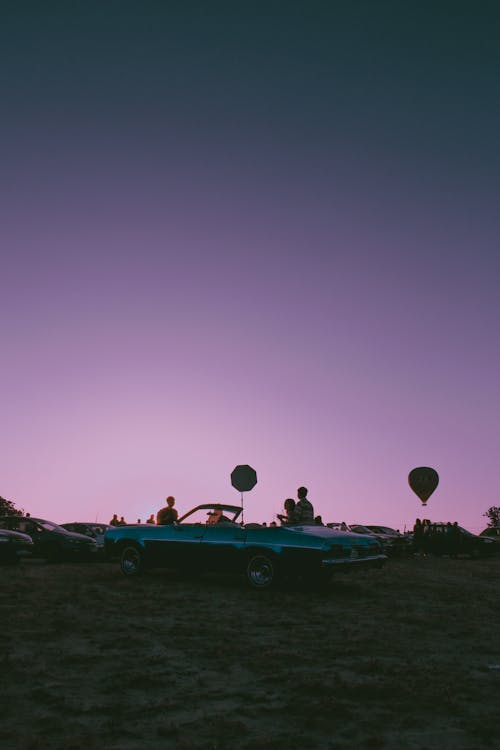 People with Vintage Cabriolet at Dusk under Purple Sky