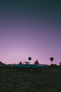 Silhouette of a vintage car against purple dusk sky with hot air balloons in Türkiye.