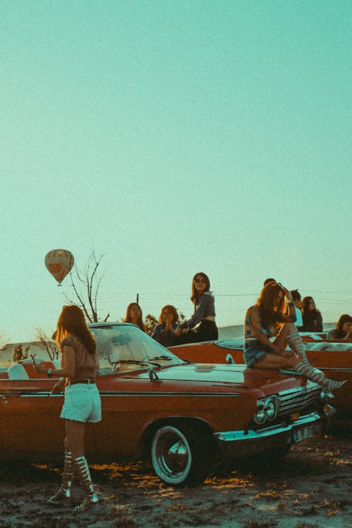 Group of Women in Rented Classic Cars Watching a Hot Air Balloons Flying over Cappadocia at Sunset