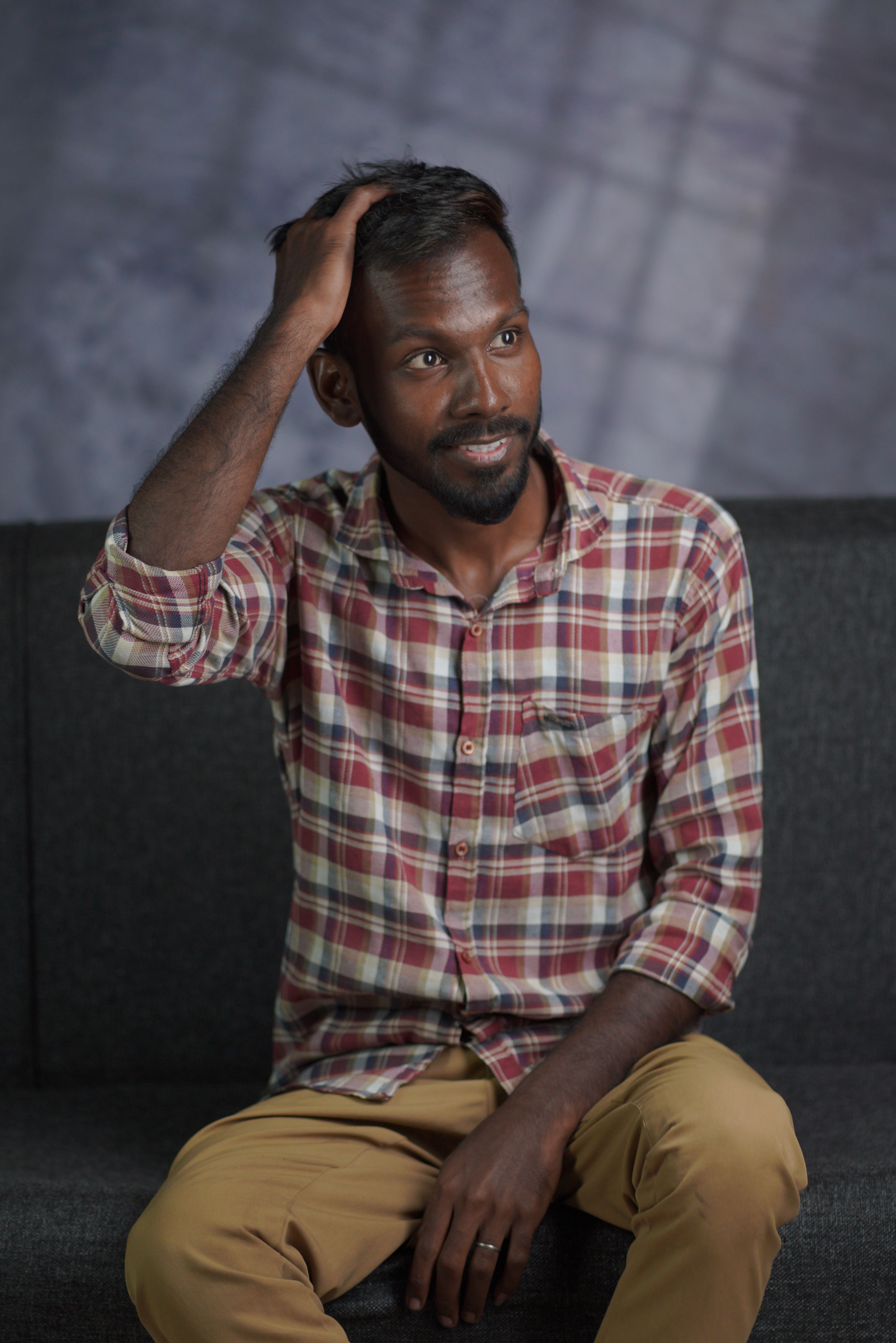A thoughtful South Asian man in a plaid shirt sitting indoors, fixing his hair.