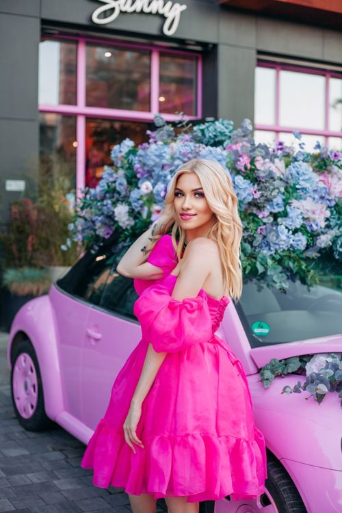 Free Blonde woman posing beside a pink car adorned with flowers in Paris. Stock Photo