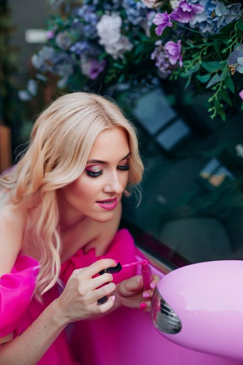 Free Blonde woman applying makeup near a pink car in Kyiv, Ukraine. Stock Photo