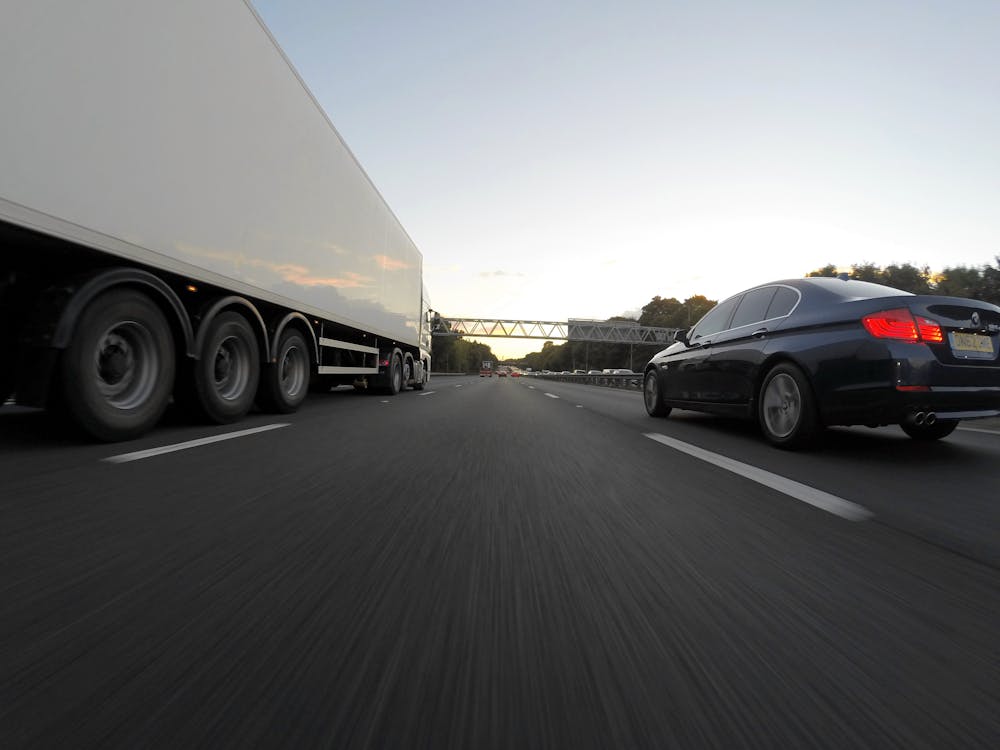 Free Blue Infiniti Sedan Running on Road Togerther With White Freight Truck Stock Photo