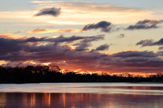 Stunning silhouette of forest and lake under a vibrant sunset sky with dramatic clouds.
