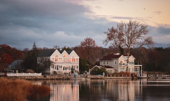 Charming waterfront residences reflecting in a calm lake, captured during a serene autumn evening.