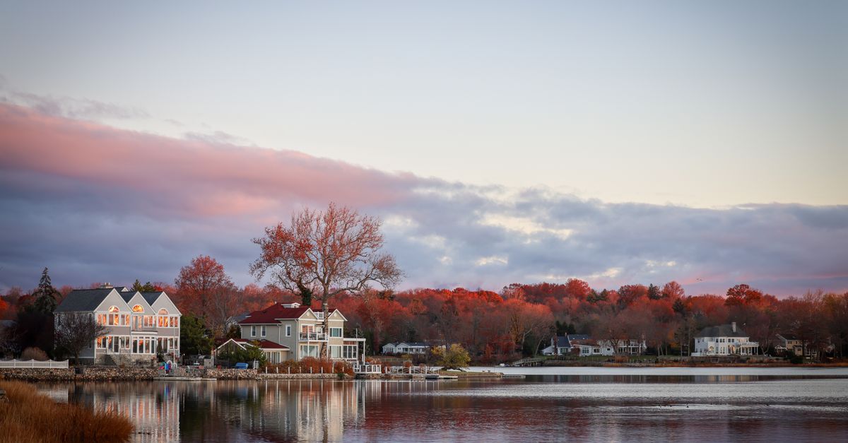Picturesque autumn lake scene with houses and vibrant foliage under a dramatic sky.