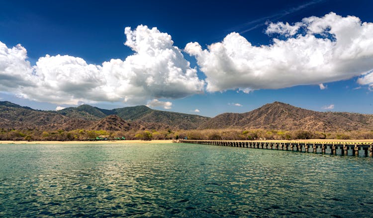 White Clouds Over Sea Coast With Pier And Hills