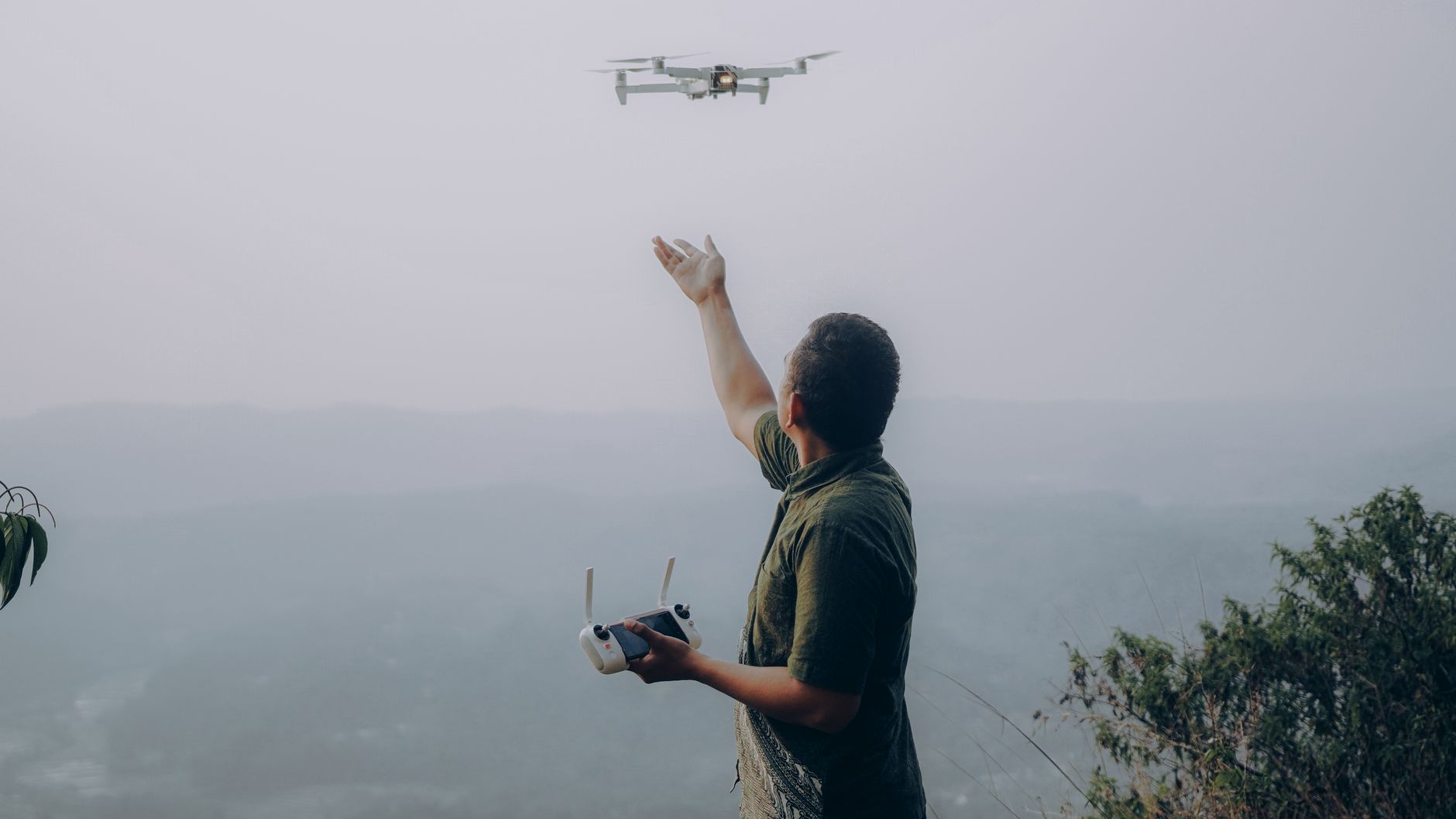 A man controlling a drone with a remote in a scenic rural area of Indonesia, showcasing modern technology.
