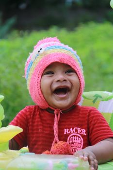 A joyful baby laughing heartily while wearing a vibrant wool hat outdoors. Capturing happiness.