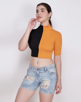 Stylish woman posing in bi-color top and ripped denim shorts against a neutral background.