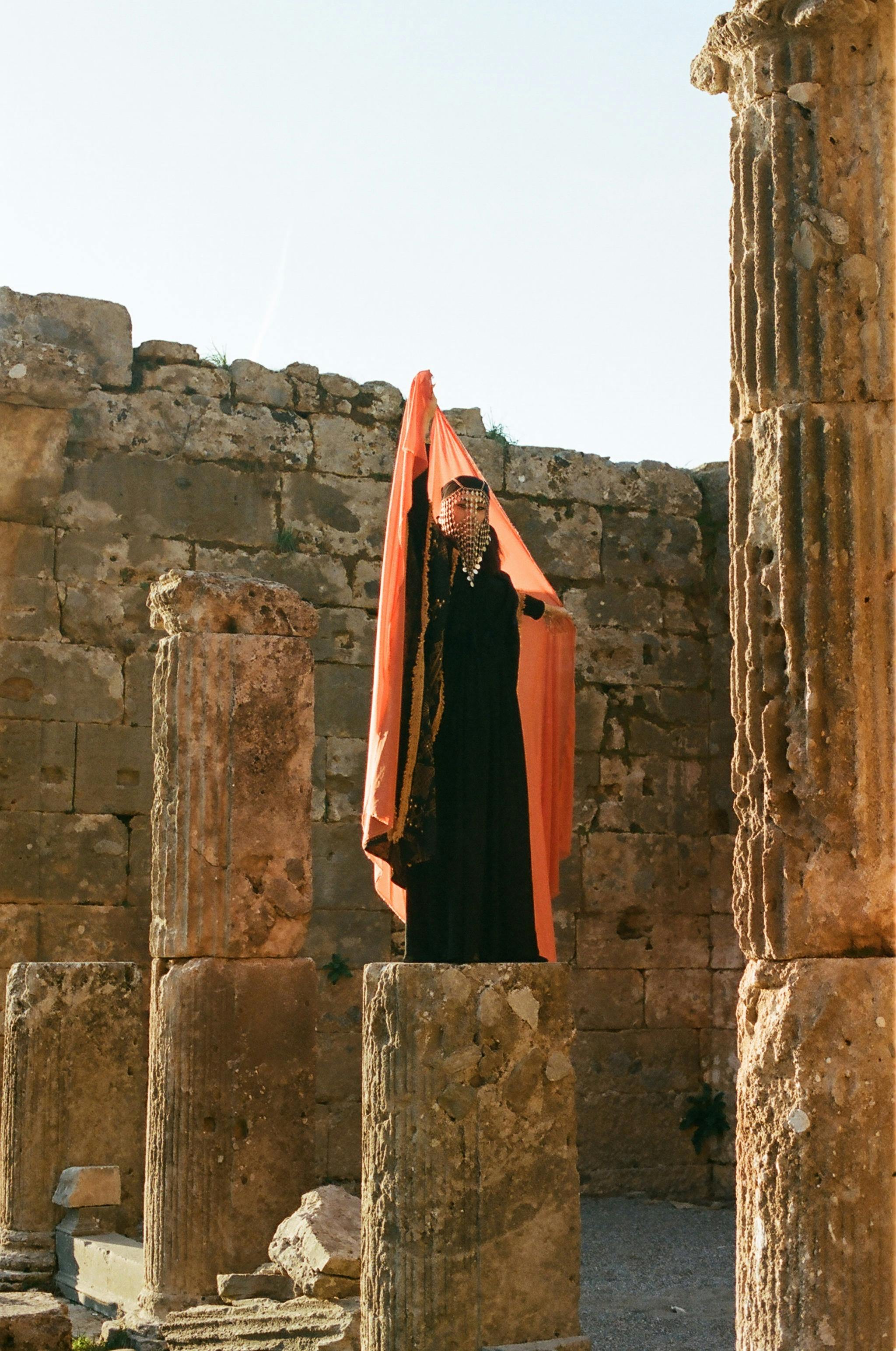 Free A woman in traditional attire poses among ancient ruins with tall columns. Stock Photo