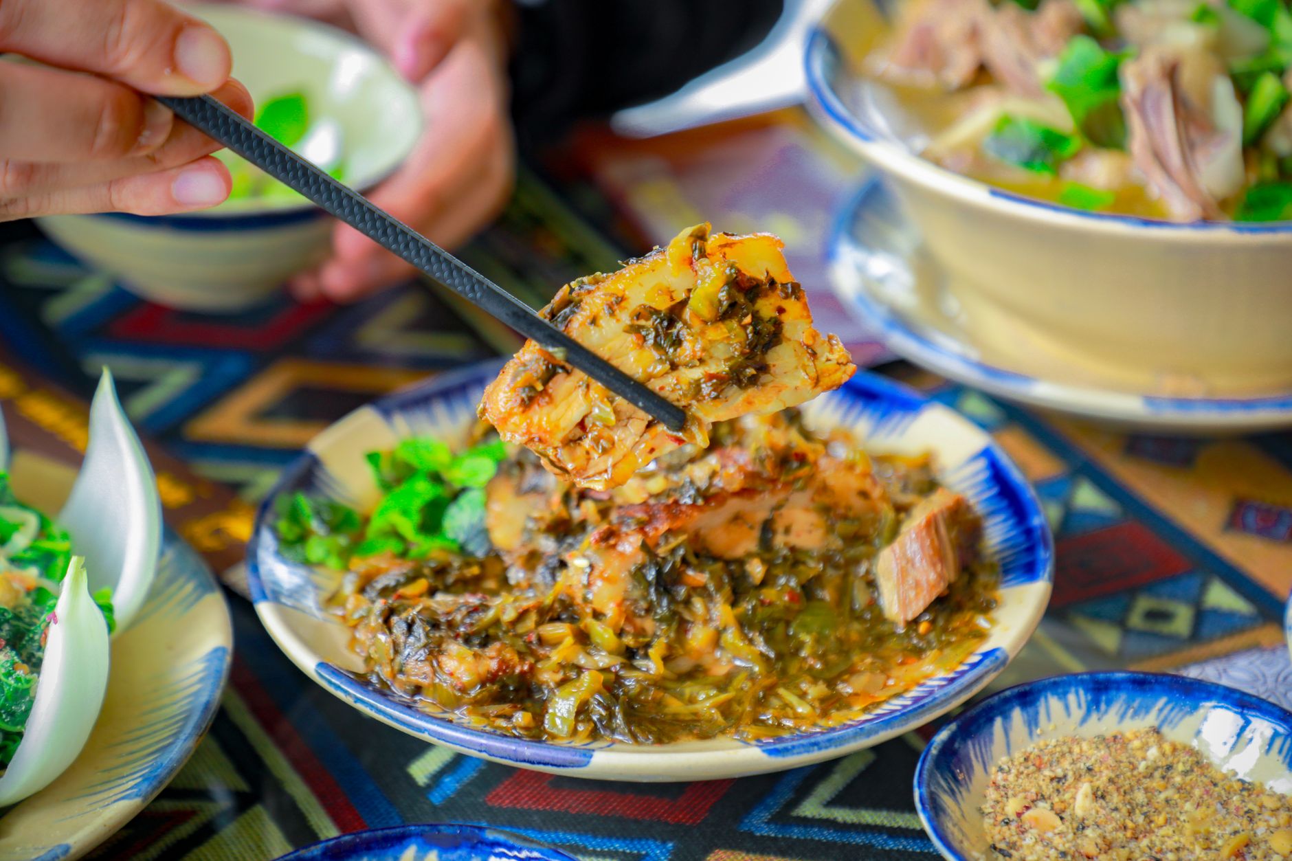 Close-up of a traditional Vietnamese pork dish with vegetables, captured indoors with chopsticks.