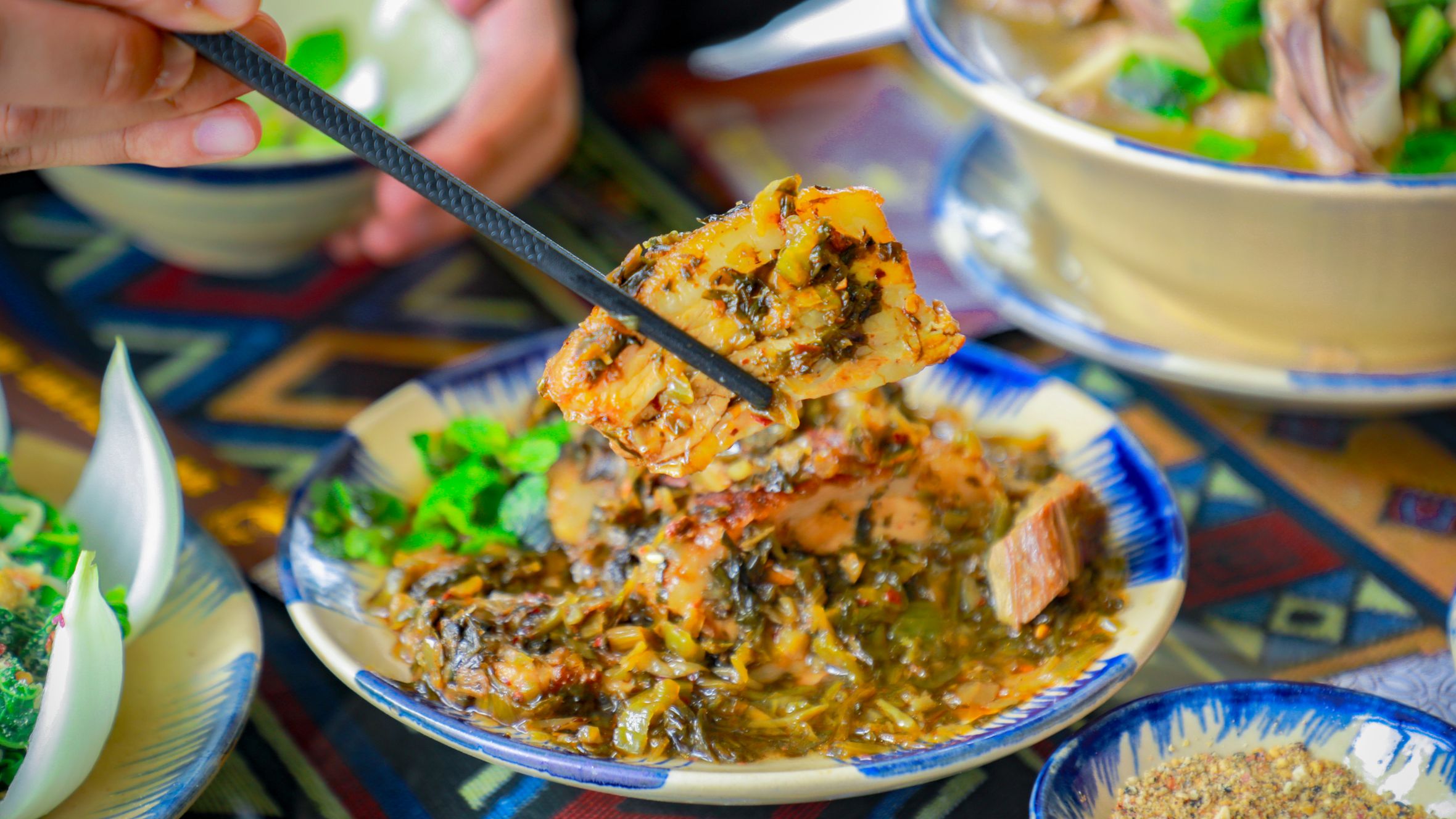 Close-up of a traditional Vietnamese pork dish with vegetables, captured indoors with chopsticks.