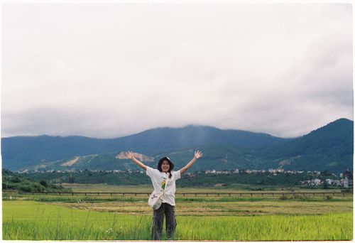 Free A cheerful woman stands with open arms in a lush green valley against a mountain backdrop. Stock Photo