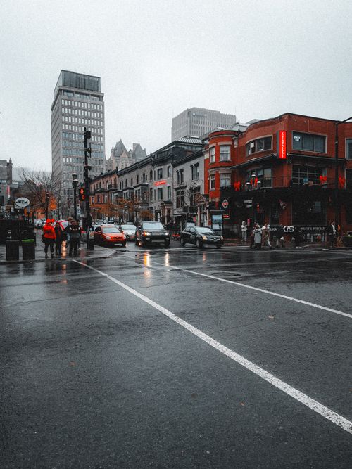Free City street scene on a wet day with cars and pedestrians under an overcast sky. Stock Photo