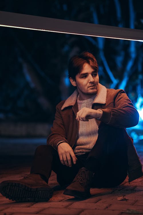 Man in Jacket and Sweater Sitting on Pavement