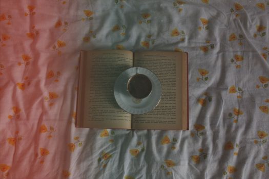 An open book with a cup of coffee on a floral patterned sheet, viewed from above.