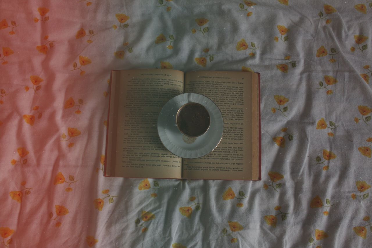 an open book with a cup of coffee on a floral patterned sheet viewed f