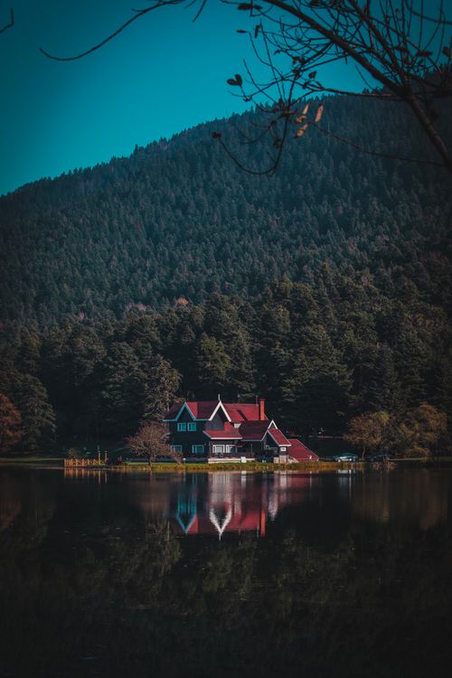 Free Picturesque house by a tranquil lake, surrounded by lush forest and clear reflections. Stock Photo