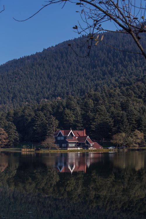 Free Idyllic house by a lake surrounded by a tranquil forest and mountain scenery. Stock Photo