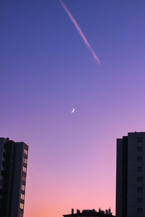 Free Serene twilight urban skyline featuring silhouetted buildings and a crescent moon against a gradient sky. Stock Photo