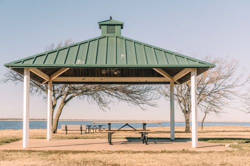 Free An empty gazebo with a green roof stands by a calm waterfront surrounded by fall trees. Stock Photo