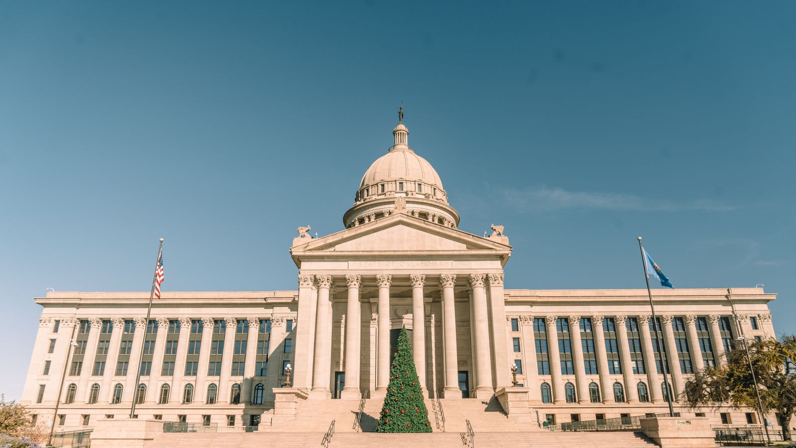 Front view of Oklahoma State Capitol adorned with a Christmas tree, under clear skies.