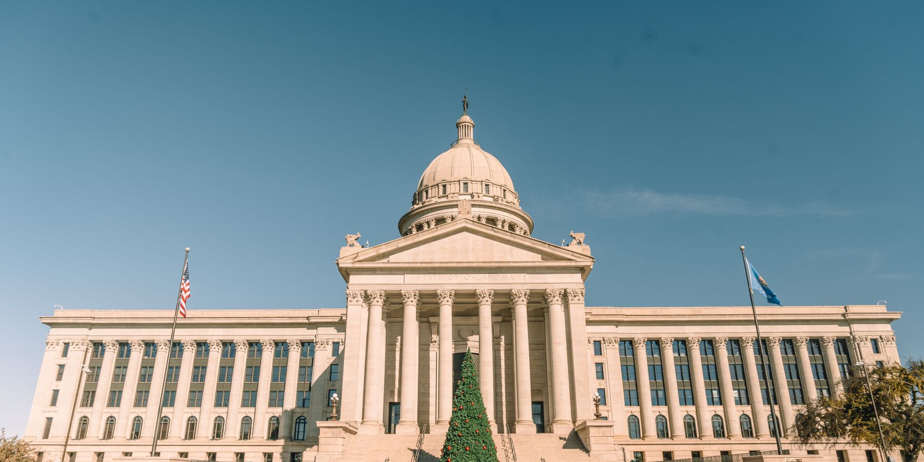 Front view of Oklahoma State Capitol adorned with a Christmas tree, under clear skies.