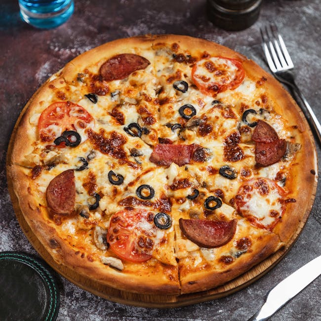 Close-up of a freshly baked Italian pizza with olives, pepperoni, and tomatoes on a wooden board.