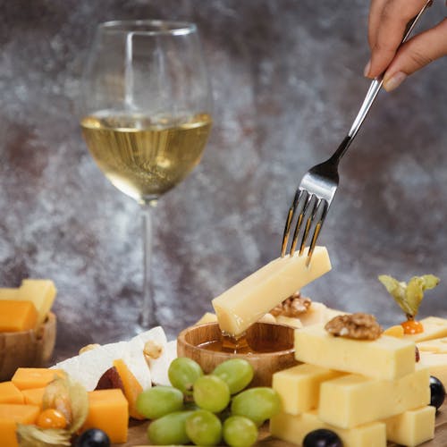 Dipping cheese into honey. Platter, snacks and white wine. Overhead