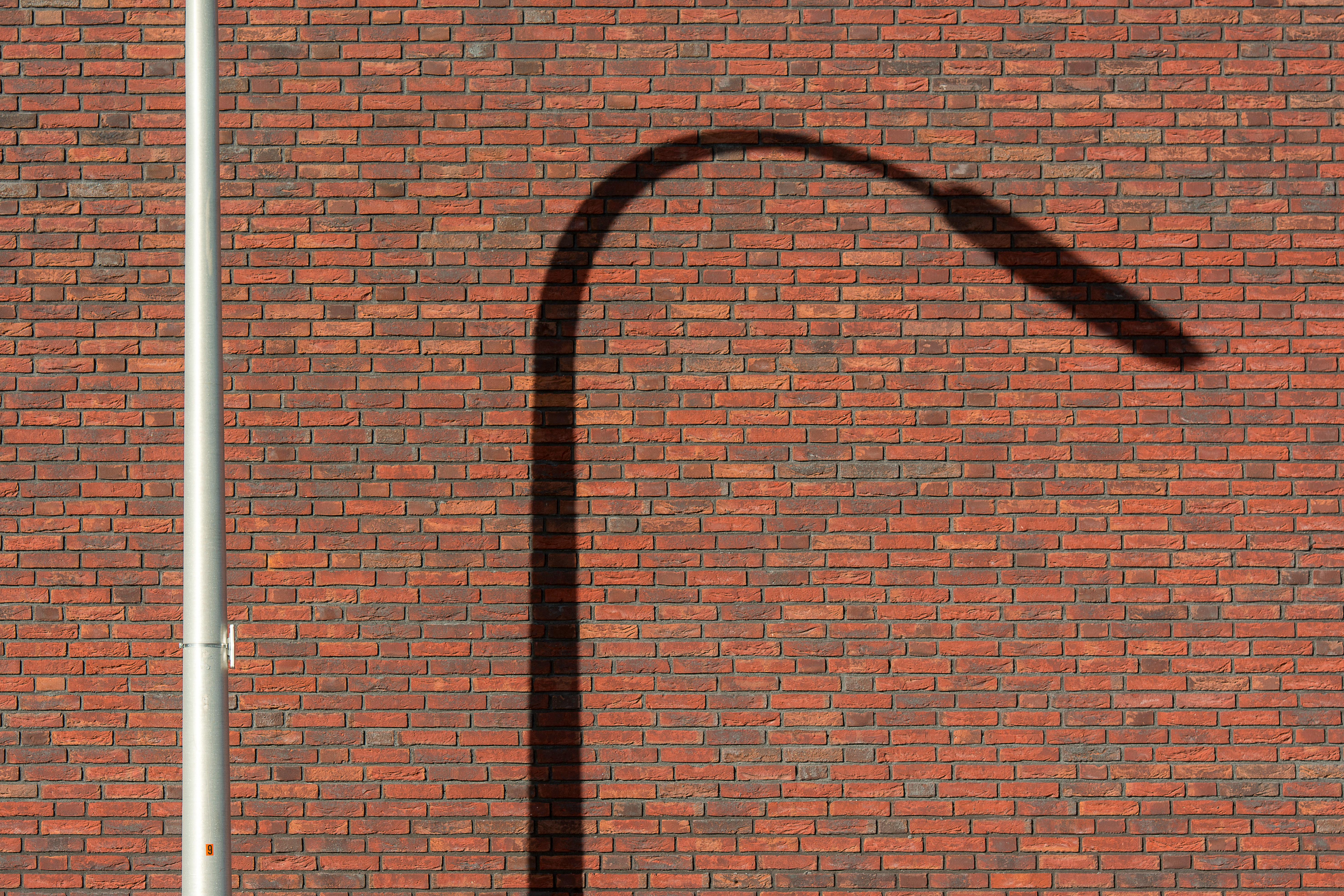 A streetlamp casts a shadow against a red brick wall in an urban setting.