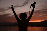 A silhouette of a person with a camera raised against a vibrant sunset sky in Kyrgyzstan.
