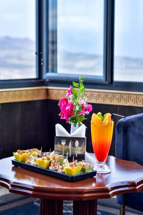 Free A colorful cocktail with appetizers and vibrant flowers on a table by a window, creating a luxurious dining ambiance. Stock Photo