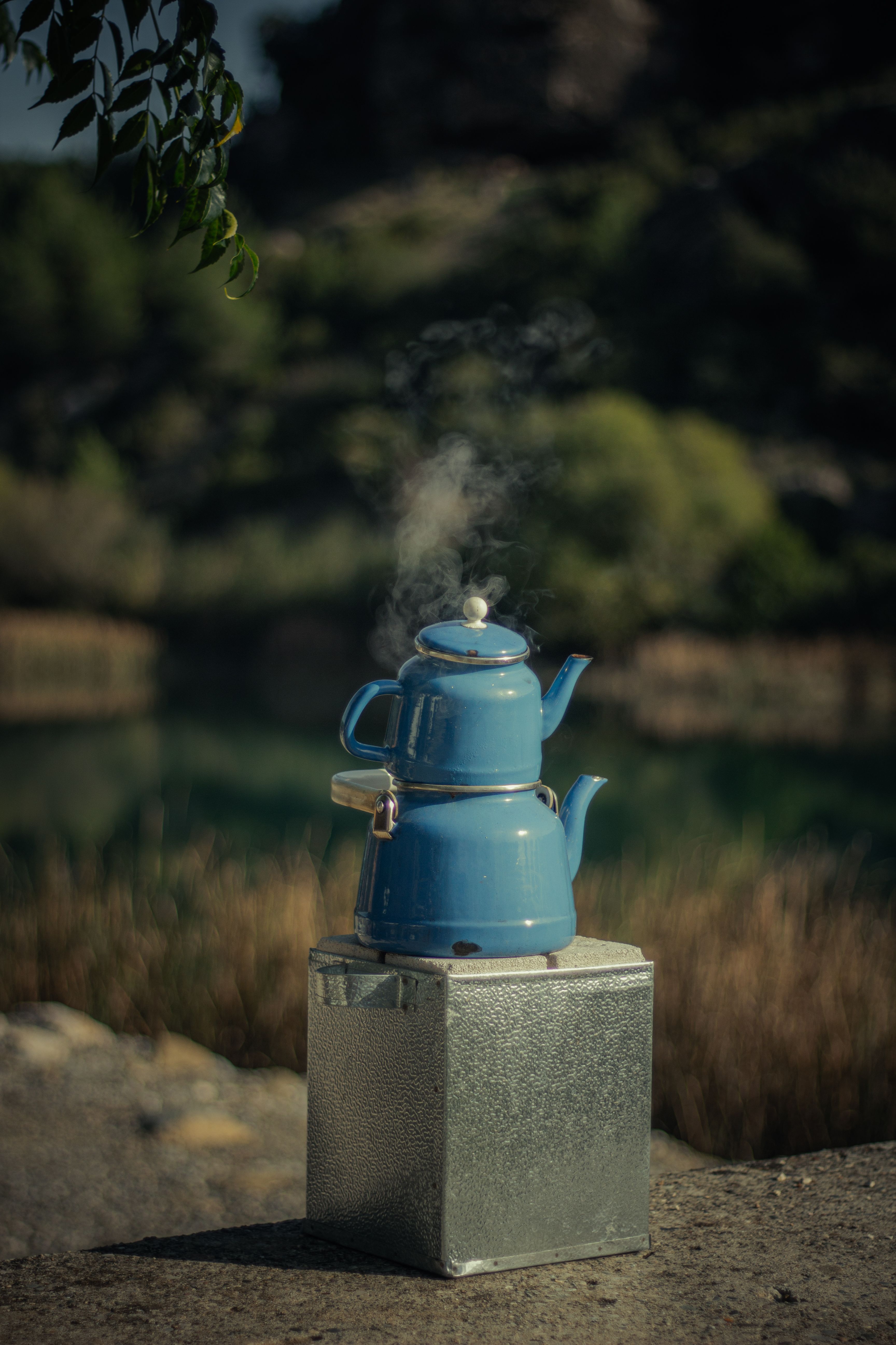Blue teapot steaming outdoors on a metal box, capturing a rustic and traditional vibe.