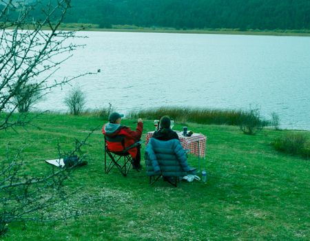 Two people enjoying a peaceful picnic by a lake, surrounded by nature.