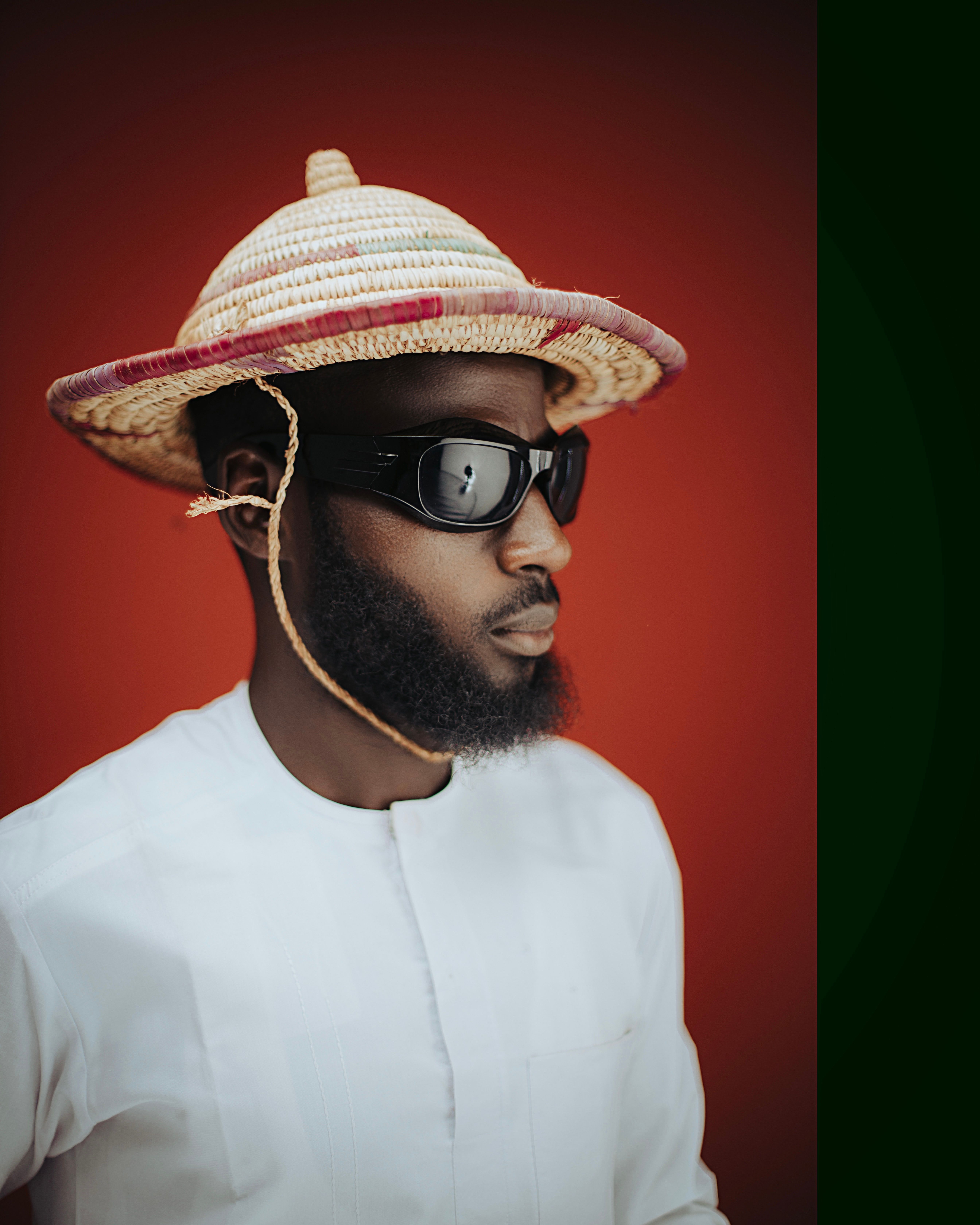 Portrait of a man wearing a straw hat and sunglasses against a red background, combining tradition and style.