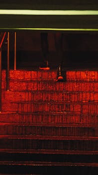 A dimly lit urban stairway illuminated by red light, creating a moody atmosphere.