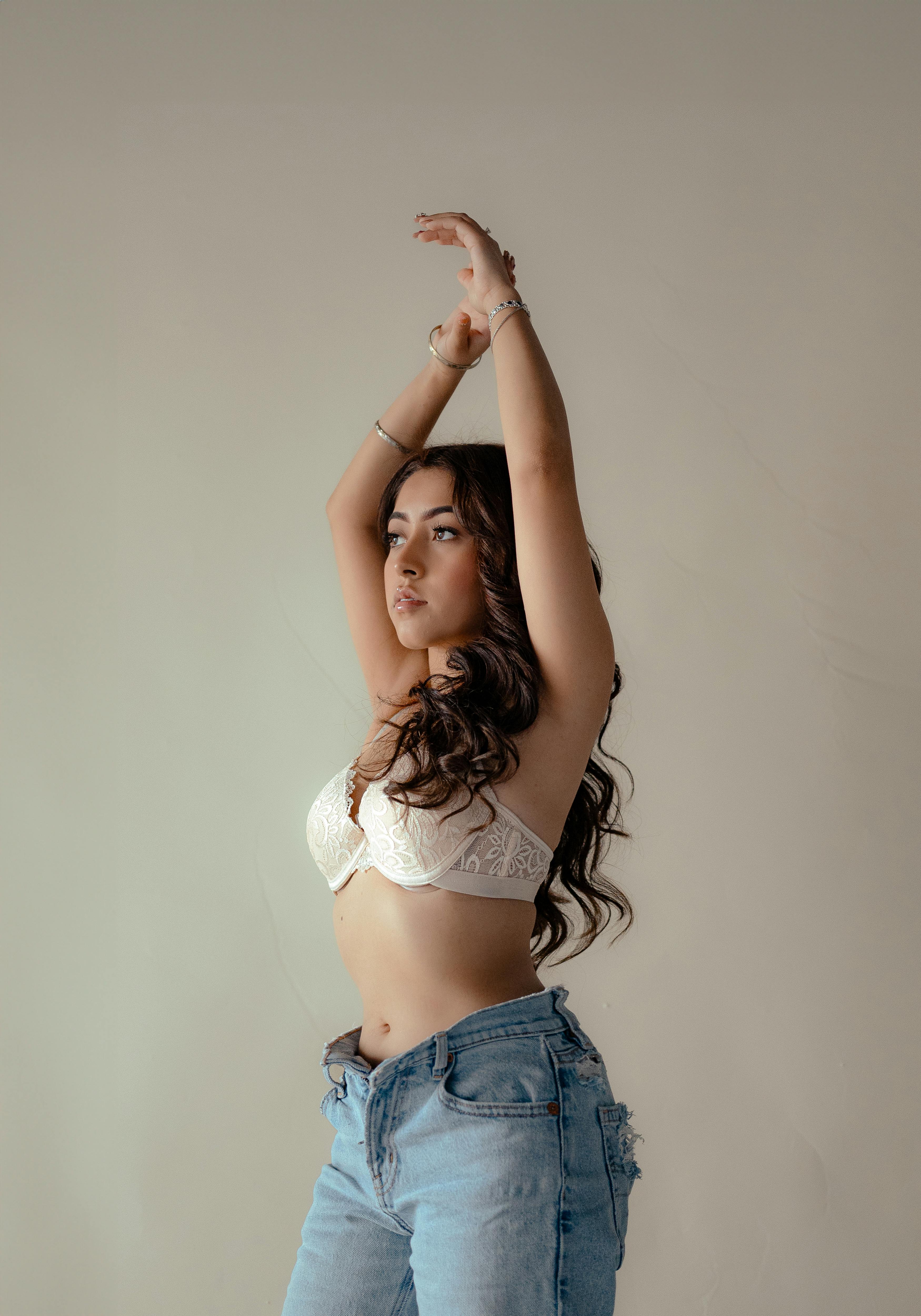 Young Woman in a Bra and Jeans Standing with her Arms Raised