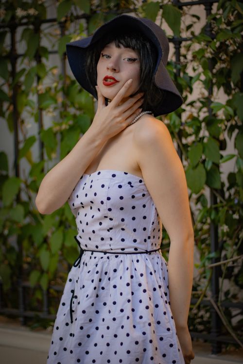 Free Stylish woman in a polka dot dress and wide-brimmed hat posing outdoors. Stock Photo