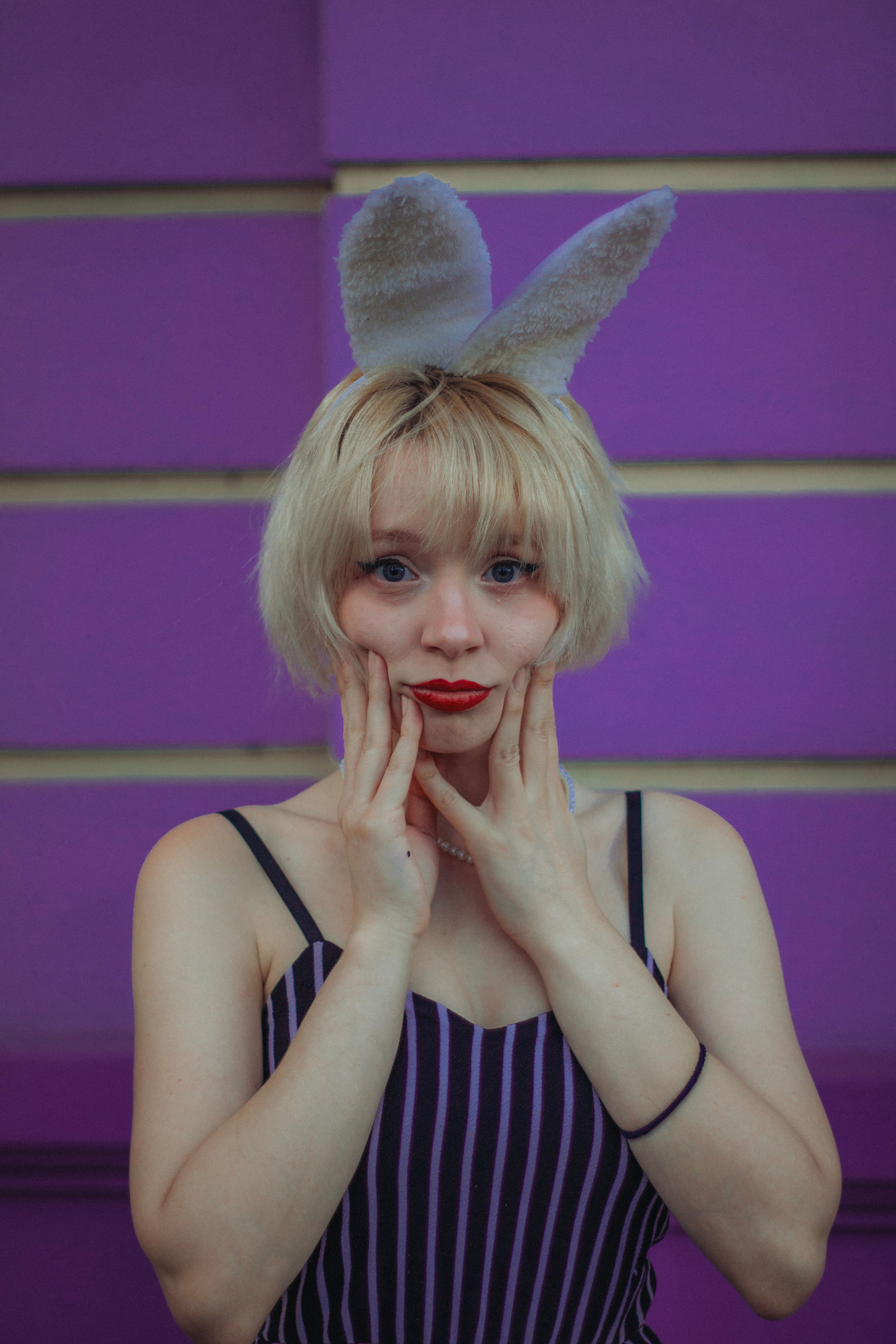 Young woman with blonde hair and bunny ears playfully posing against a vibrant purple wall.