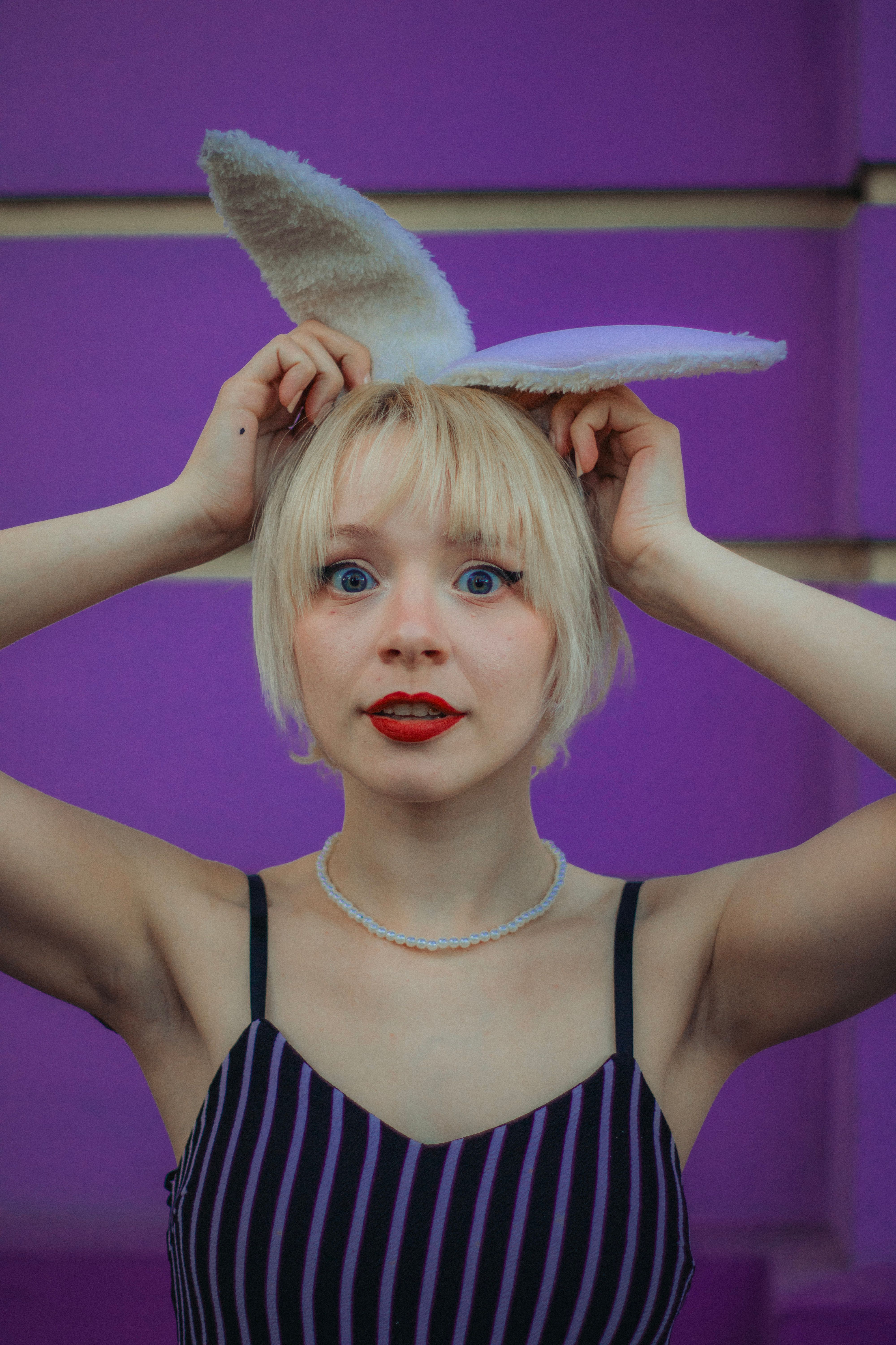 A playful portrait of a blonde woman with bunny ears against a vibrant purple background.