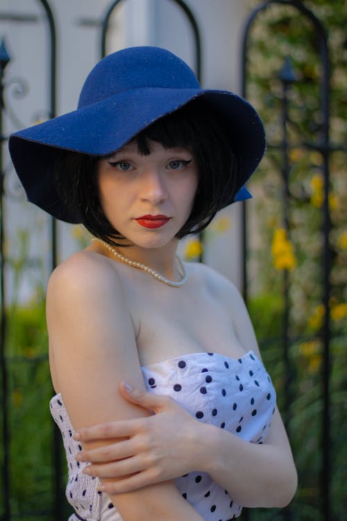 Young Woman Posing Outside in a Dotted Dress and a Hat 